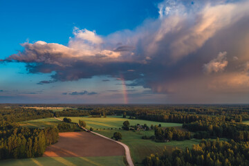 landscape with storm clouds and rainbow over countryside road and fields