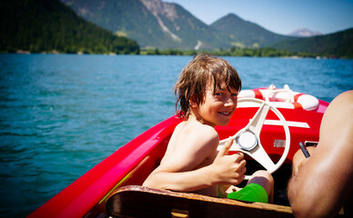 Boy on red boat on sky blue lake in summer in Tyrol, Austria 