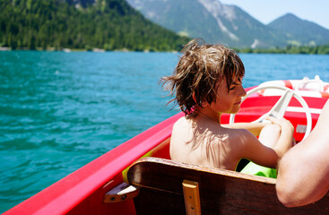 Boy on red boat on sky blue lake in summer in Tyrol, Austria 