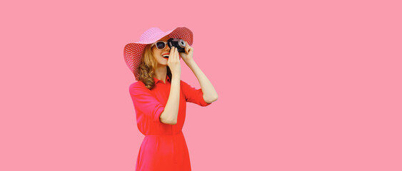 Summer portrait of happy smiling young woman photographer with film camera wearing straw hat, pink dress, sunglasses on background