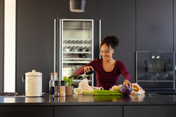 Happy biracial woman unpacking groceries in kitchen