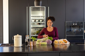 Happy biracial woman unpacking groceries in kitchen