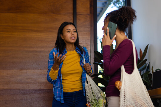 Happy biracial lesbian couple coming home from shopping and talking on smartphone