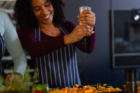 Happy biracial lesbian couple seasoning vegetables in kitchen