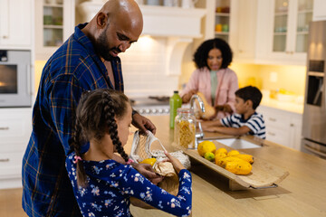 Happy biracial parents, son and daughter unpacking grocery shopping in kitchen