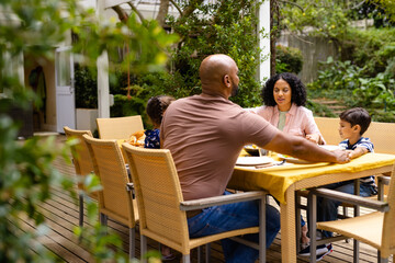 Happy biracial parents, son and daughter praying before meal, holding hands at table in garden