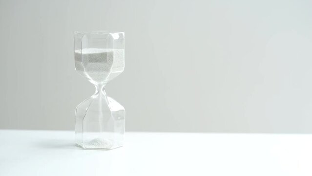 Hourglass on a white table and a light background. Faceted and co with light gray sand