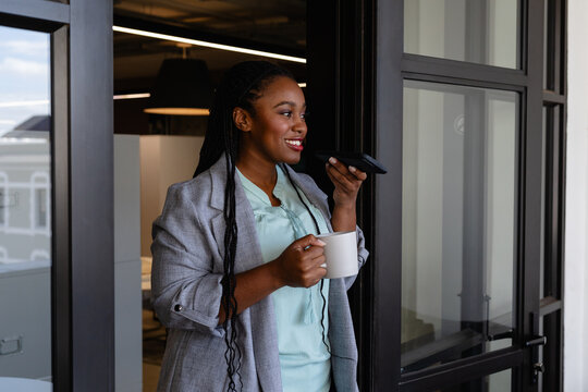 Plus size african american casual businesswoman with cup of coffee talking on smartphone in office