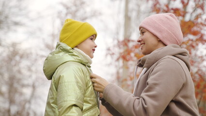 Mom takes care of girl child on street. Family health concept, warm clothes outdoors in autumn, kid...