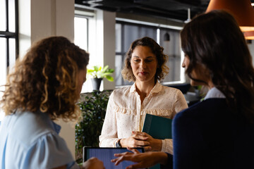 Diverse female colleagues in discussion using tablet in casual office meeting