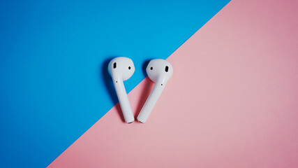 White wireless earphones on blue and pink background.