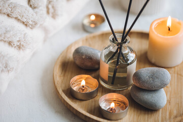 Burning candles on bamboo tray, cozy home atmosphere. Relaxation, detention zone in the living or bedroom. Stones, sea shells as decor. Apartment natural aroma diffusor with ocean breeze fragrance. - obrazy, fototapety, plakaty