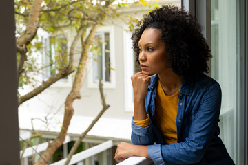 Fototapeta na wymiar Thoughtful biracial woman with black curly hair looking out window at home