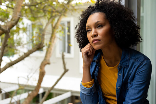 Thoughtful Biracial Woman With Black Curly Hair Looking Out Window At Home