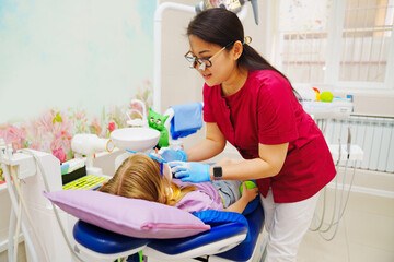 A pediatric dentist treats or performs oral hygiene for a little girl.