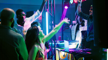 Multiethnic group of adults partying and dancing on club music, having fun at discotheque with DJ...