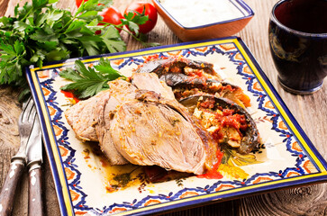 Traditional roasted Greek lamb roast with eggplant and feta cheese in tomato sauce served as close-up on a rustic design plate