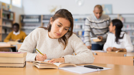 Interested young Latina spending time in library, reading books and making notes. Self-education concept