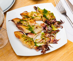 Roasted calamari with pesto sauce dished up in a plate on the laid restaurant table