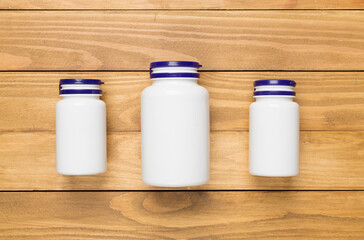 Plastic bottles with vitamins on wooden background, top view