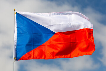 Large flag of Czech Republic fixed on metal stick waving against background of cloudy sky during daytime
