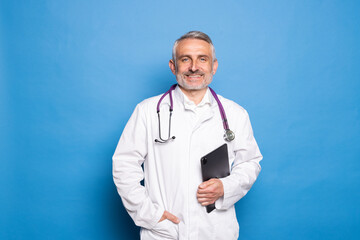 Friendly middle aged man in white robe wearing eyeglasses with stethocsope on his chest doctor holding digital tablet