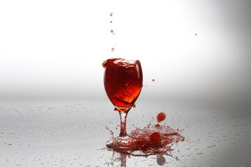 Copa de vino sobre un fondo blanco con sombras haciendo un charco con el vino que se derrama