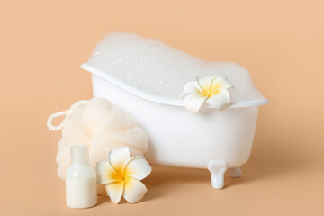 Obraz na płótnie Canvas Small bathtub with foam, flowers, sponge and bottle of cosmetic product on color background