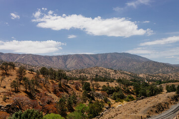 Fototapeta premium A beautiful American landscape with mountains, trees, and country houses in California on sunny days with blue sky. Bakersfield, California, USA - 7-22-2021