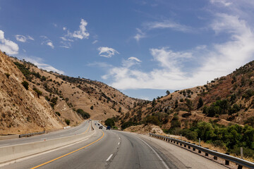 A beautiful highway among mountains with cars and trucks on sunny days. A landscape with transport. Bakersfield, California, USA - 7-22-2021