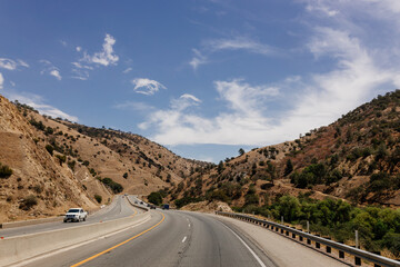 Fototapeta premium A beautiful highway among mountains with cars and trucks on sunny days. A landscape with transport. Bakersfield, California, USA - 7-22-2021
