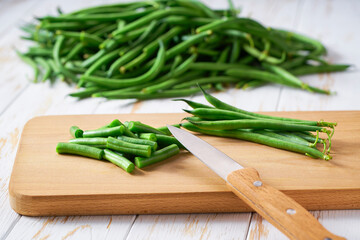 Whole and chopped green beans on a cutting board, close up.