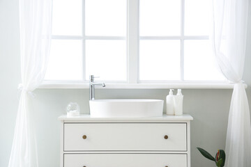 White sink with bath accessories on chest of drawers and window in room