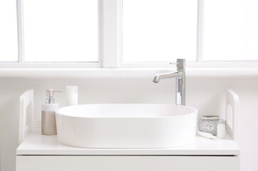 White sink with bath accessories on table in light bathroom