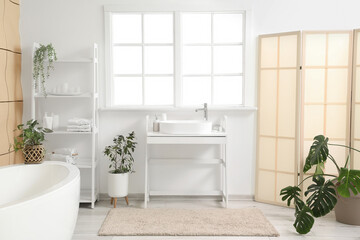 Fototapeta na wymiar Interior of light bathroom with sink, bathtub, shelving unit and houseplants