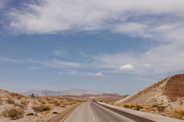A beautiful asphalt road among hills with dry grass. A scenic landscape with highway, mountains on background and blue sky with fluffy clouds on sunny day. Bakersfield, California, USA - 7-22-2021