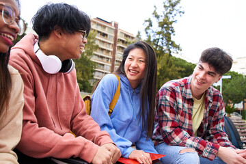 Group of four students laugh and have fun outdoors. Gen z multi-ethnic classmates are happy and cheerful sitting in a bench of the campus. Smiling teens at break of university or high school