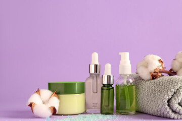 Cosmetic products, clean towel and cotton flowers on lilac background, closeup
