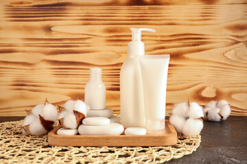 Fototapeta na wymiar Bottles of cosmetic products, spa stones and cotton flowers on table against wooden background