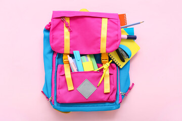 Color school backpack with notebooks and stationery on pink background