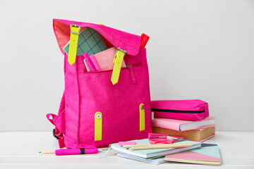 Pink school backpack with books, pencil case and stationery on white wooden table near wall