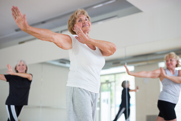 Fototapeta na wymiar Energetic elderly woman practicing modern vigorous dance movements in group dance class .