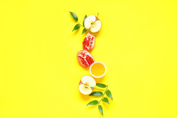 Composition with fresh apple, pomegranate, honey and plant leaves on yellow background. Rosh hashanah (Jewish New Year) celebration
