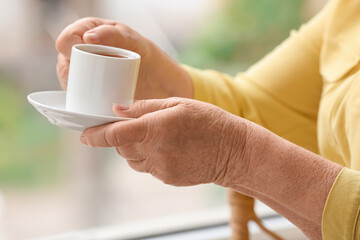 Senior woman with cup of coffee at home, closeup