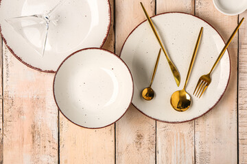 Clean plates with set of golden cutlery on beige wooden table