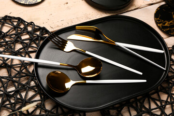 Clean plate with set of golden cutlery and black place mats on beige wooden table