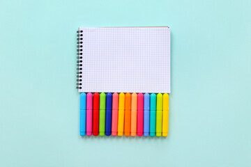 Blank notebook with different colorful markers on blue background