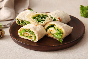 Plate of tasty lavash rolls with egg and greens on light background