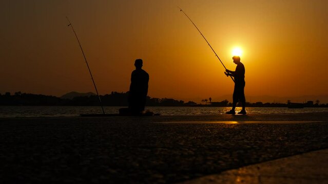Have friend time with fishing by river. A view of people silhouettes catch the fish on the river bank during evening time in summer.