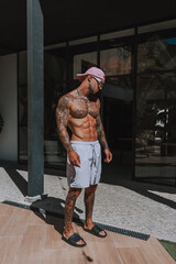 Fototapeta na wymiar Chico joven tatuado y musculoso posando con bañador urbano en piscina de hotel un día soleado